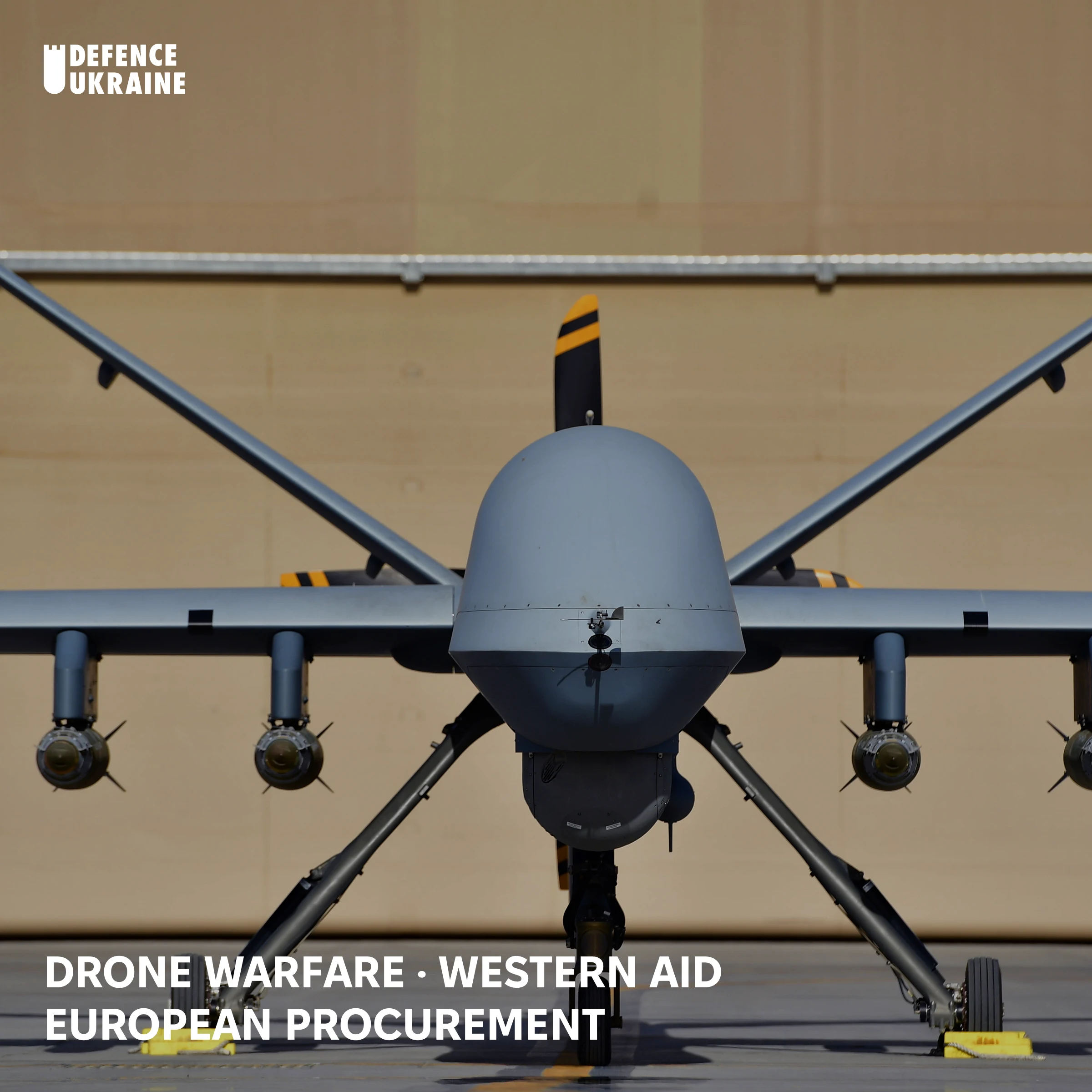 An MQ-9 Reaper drone parked head-on in a sunlit hangar, four AGM-114 Hellfire missiles mounted under its wings.